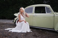 a woman in a white dress sitting next to a vw beetle